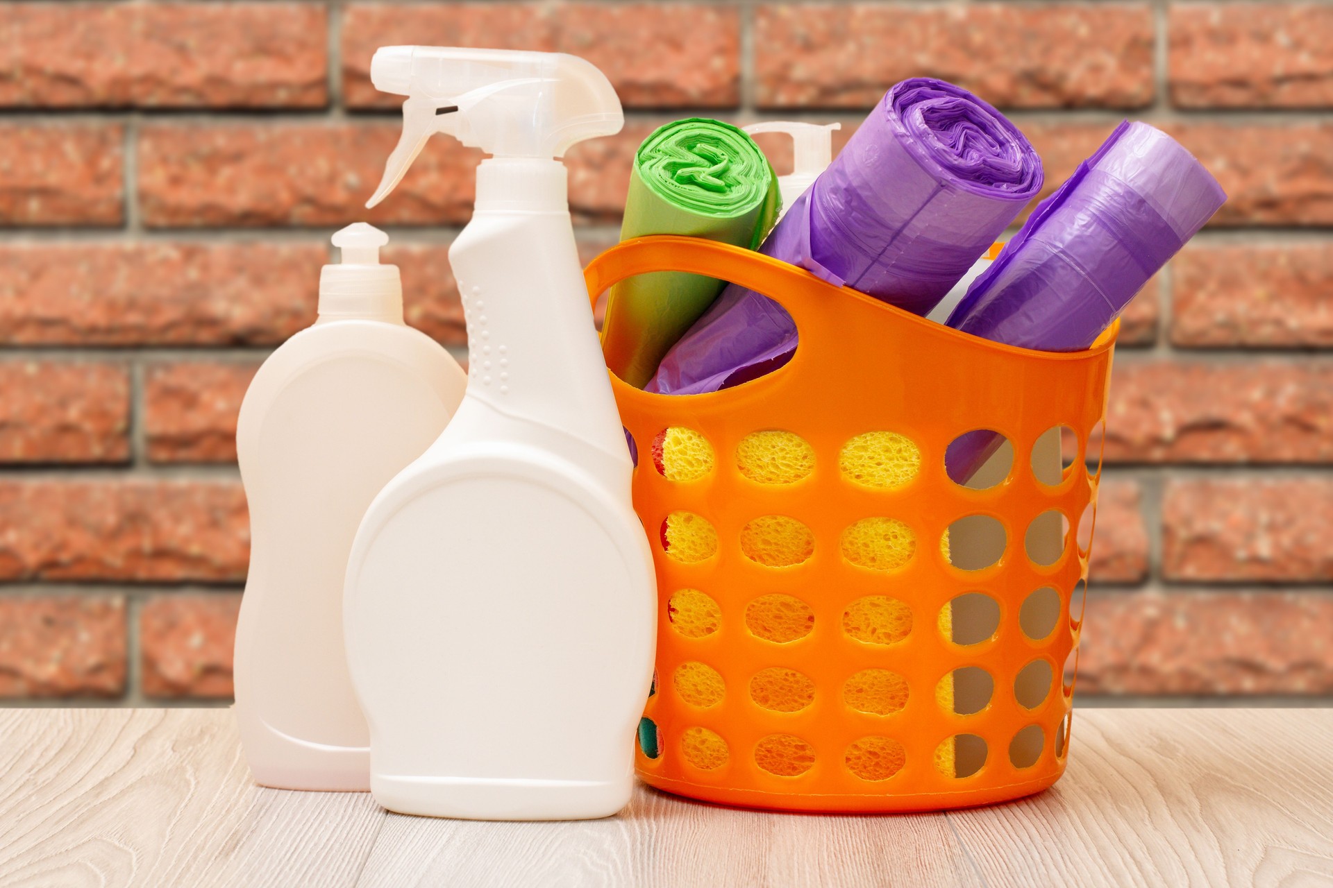 Botellas de líquido lavavajillas, cesta con bolsas de basura y esponjas.